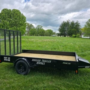 A black trailer sitting in the grass next to trees.