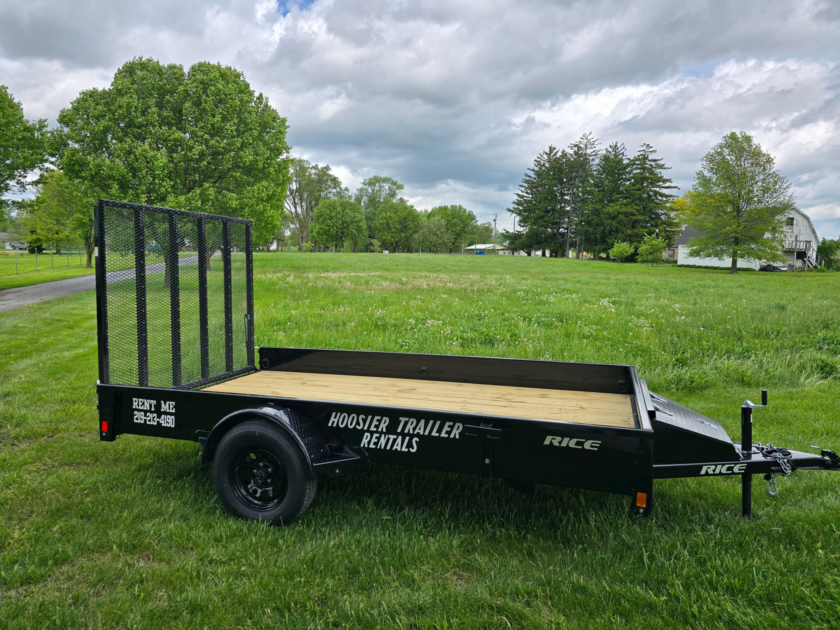 A black trailer sitting in the grass next to trees.