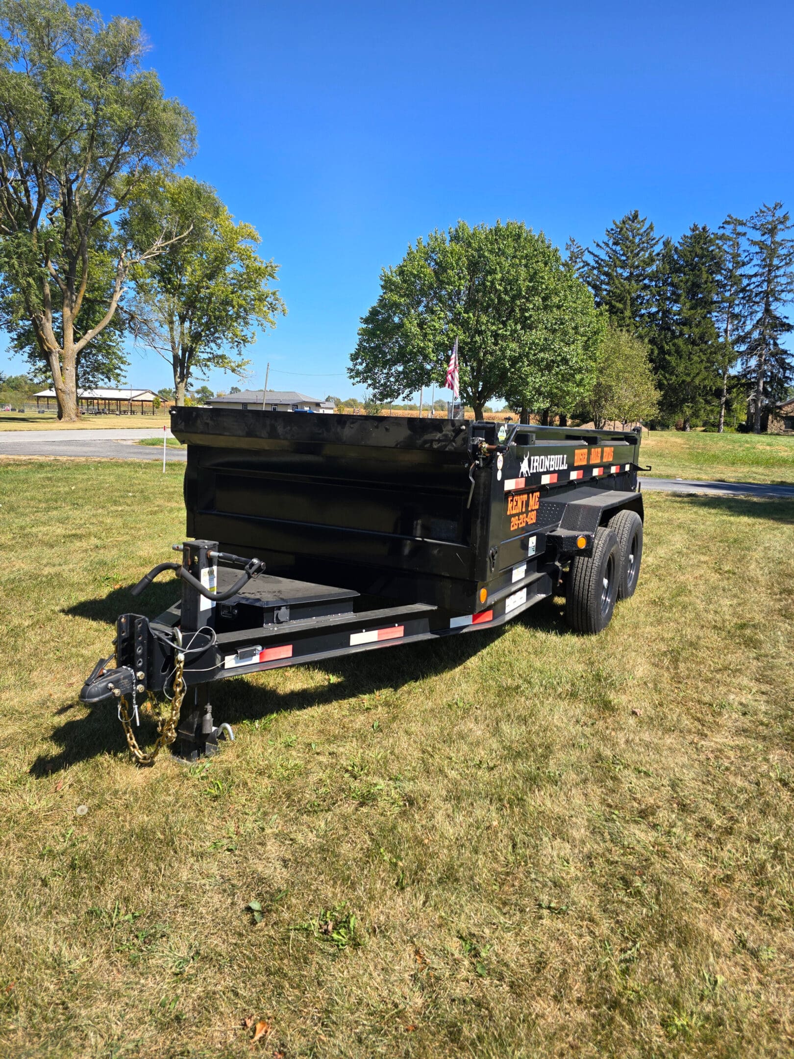 A dump trailer sitting in the grass near some trees.
