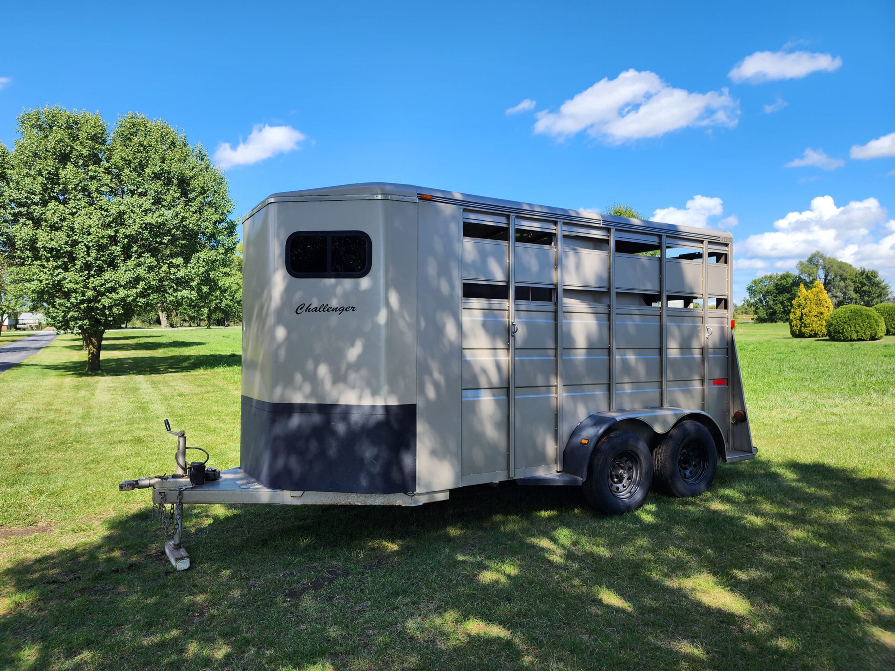 A horse trailer parked in the grass near some trees.