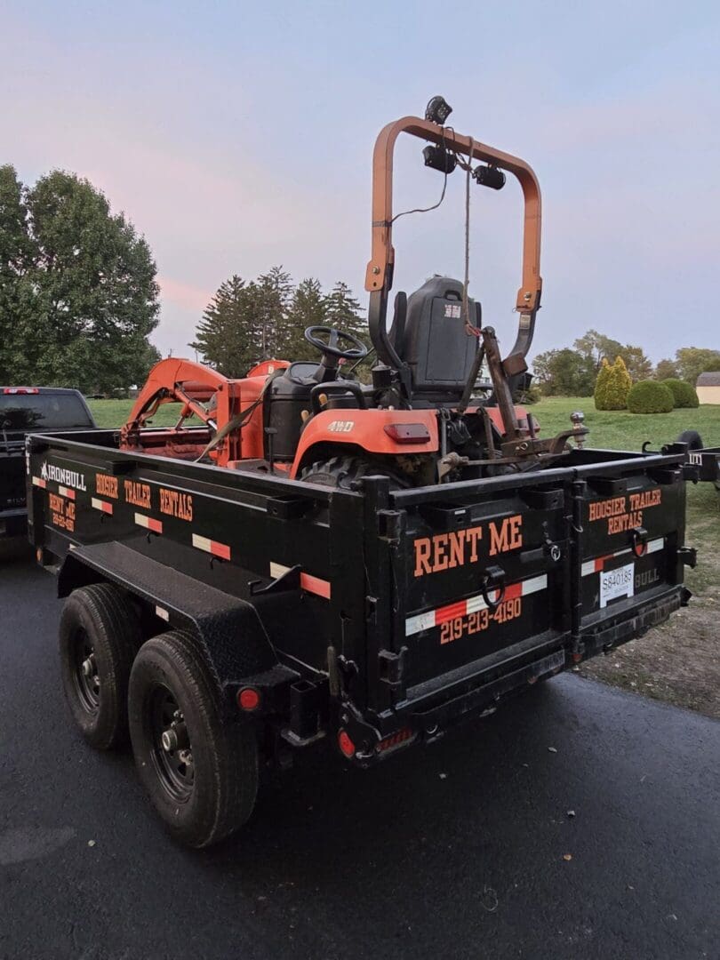 A black trailer with an orange tractor on it.