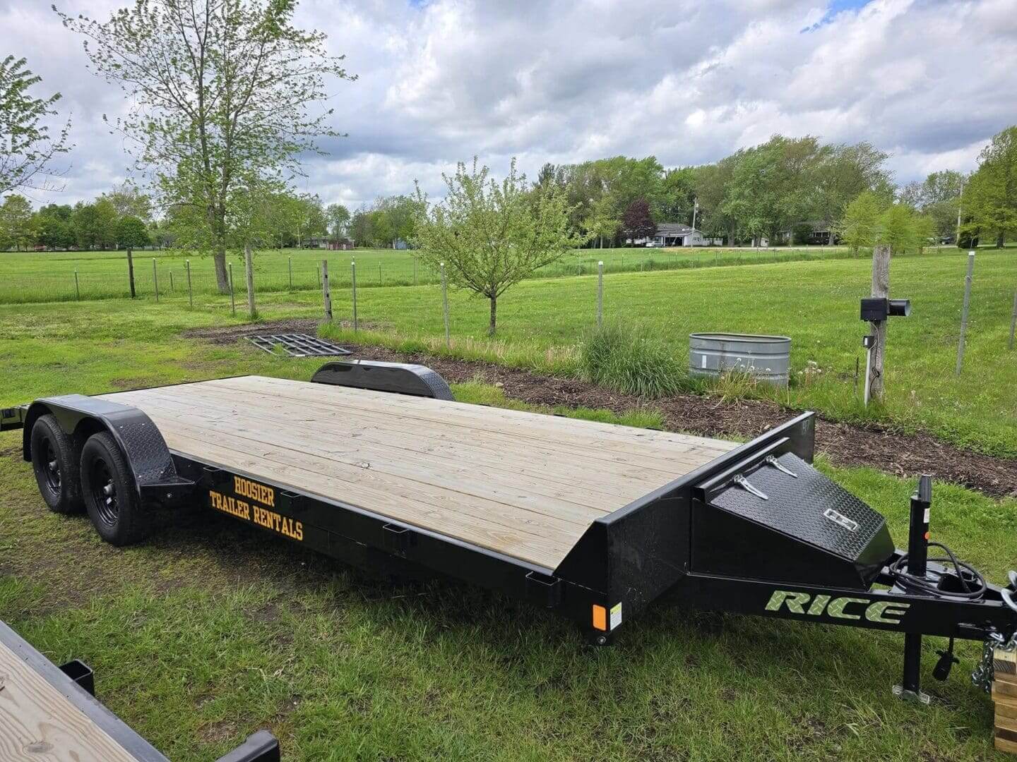 A black trailer with wooden deck sitting in the grass.